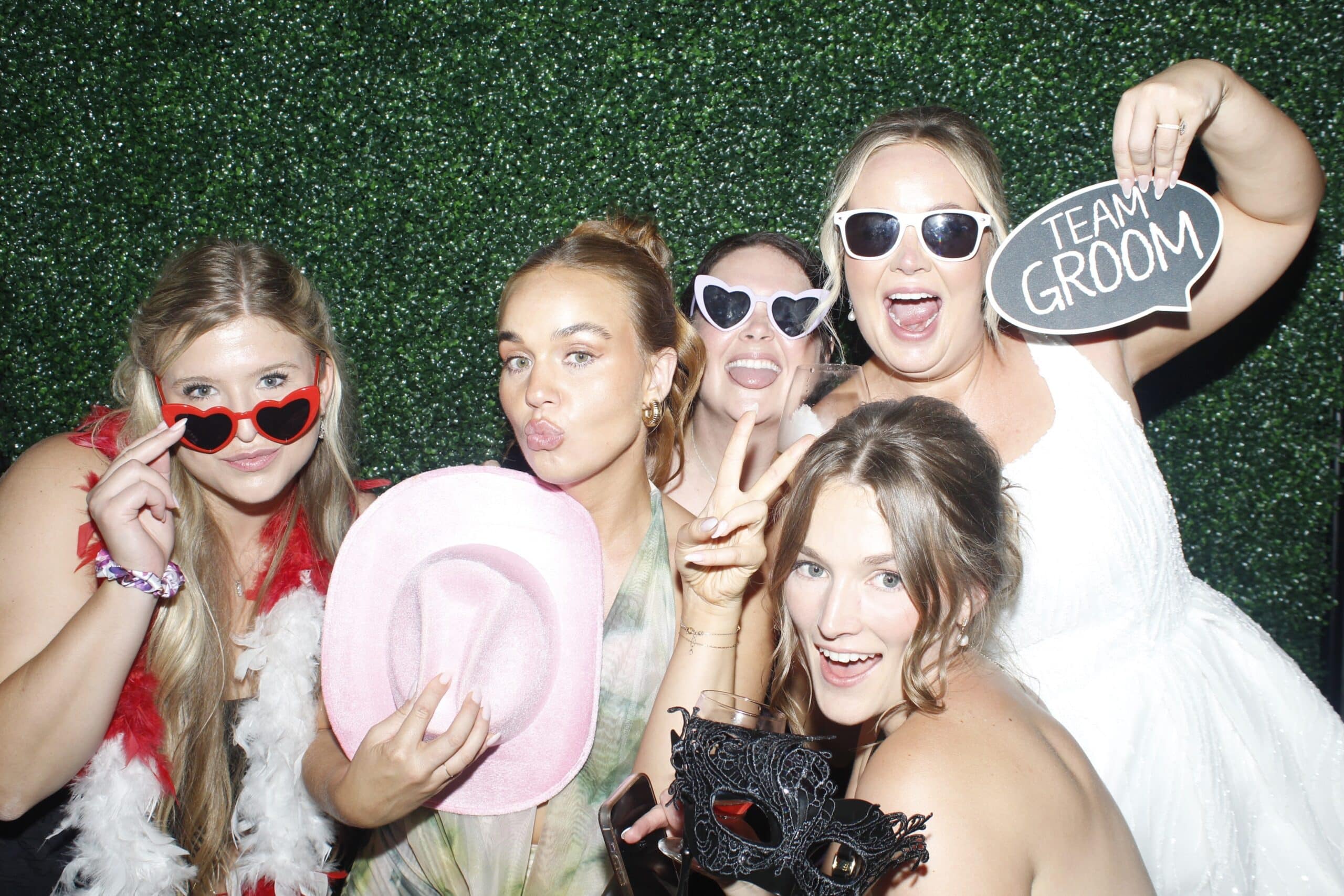 Wedding guests and bridge using photobooth with greenery wall
